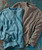 Past In The Present, two textured long-sleeve shirts, one in light blue and one in gray, with button details on the front, laid out on a rustic surface.