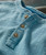 Past In The Present, close-up of a light blue textured shirt with beige buttons and a collar detail.