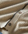 Cast Away, close-up image of a beige textured fabric with two buttons on a knitted cardigan or sweater.