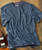 Blues & Tonic, blue checkered casual t-shirt with a front pocket, laid flat on wooden surface with guitar nearby.