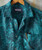 Lion Tamer, a teal tropical print button-up shirt with a front pocket containing a pen and sunglasses.