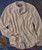 Drifting, a beige striped button-up shirt with a single chest pocket, spread out on a textured blue and rust-colored background.