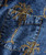Palm Wine, close-up of denim jeans with intricate gold embroidery design and a front pocket with a button.