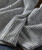 Waves Within, close-up of a soft, striped grey and white fabric with a textured pattern and folded edge.