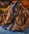 Watch Me Gone, Brown distressed leather jacket with multiple zipper pockets layered over a blue shirt and graphic T-shirt, placed on a surface with a guitar and vintage suitcase in background.