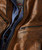 Watch Me Gone, Close-up of a brown leather jacket showcasing a zipper pocket and layered blue and patterned shirt underneath.