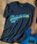Blue Guitar Blues T-shirt, dark blue T-shirt with a graphic of a blue guitar and the words 'Keeping the Blues Alive' in blue and yellow colors, next to a blue electric guitar on a wooden surface.