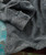Black Diamond Bay, a close-up image of a textured gray knitted sweater with detailed patterns and a buttoned cuff.