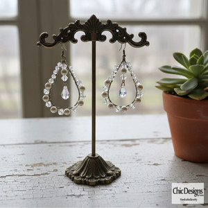 Swarovski Crystal Pear Shaped Dangle Earrings hanging from antique earring stand on a white distressed table Swarovski Crystal Pear Shaped Dangle Earrings hanging from antique earring stand on a white distressed table