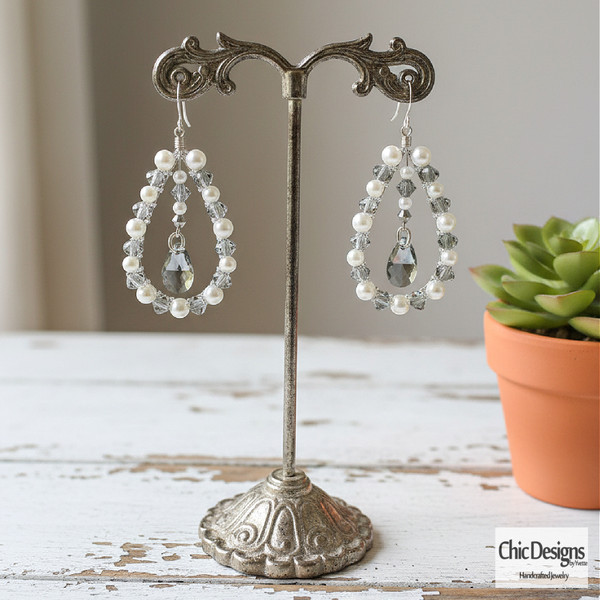 Silver Jet and Pearl Swarovski Crystal Pear Earrings standing on a distressed white table hanging from an antique earring stand