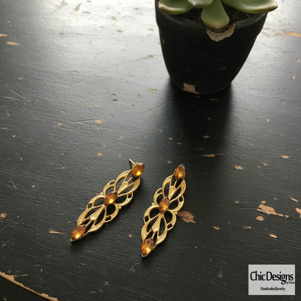 Amber Swarovski Rhinestone Filigree Pendant Earrings laying on a black distressed table