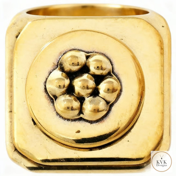 A chunky, square gold ring with a raised cluster of seven small gold spheres in the center. The design is bold and geometric. The logo "KVK Designs" appears in the bottom right corner.