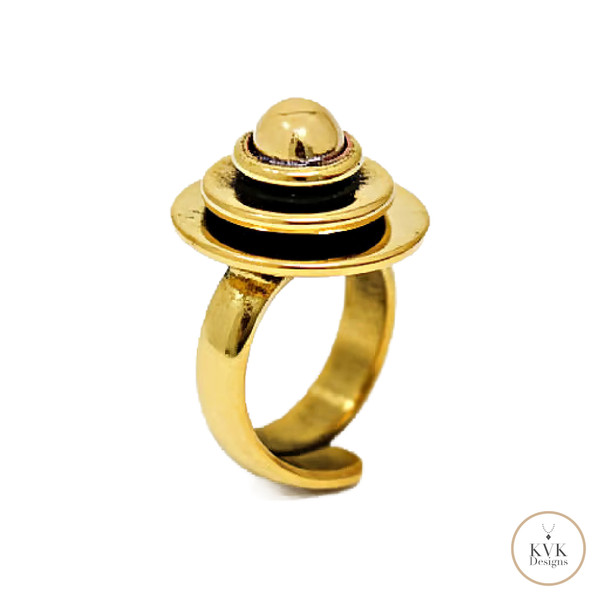 A modern gold ring featuring a circular, layered design with black enamel accents, resembling a planet with rings. The ring is displayed on a white background with a small "KVK Designs" logo in the corner.