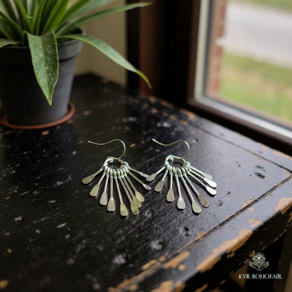 Boho Silver Metal Fringe Paddle Earrings laying on a black antique table with a plant on the table