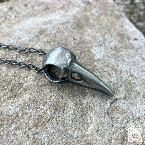 Silver Crow Skull Necklace Pendant sitting on a rock