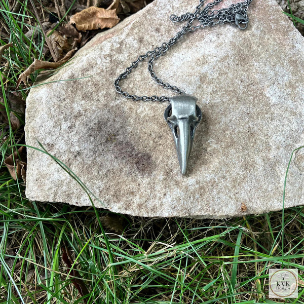 Silver Crow Skull Necklace Pendant sitting on a gray rock
