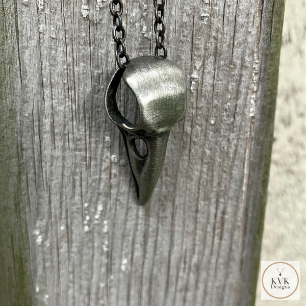 Silver Crow Skull Necklace Pendant hanging from an antique wood door