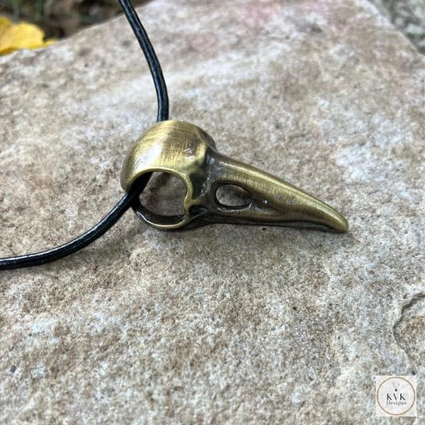 Brass Crow Skull Necklace Pendant sitting on a rock
