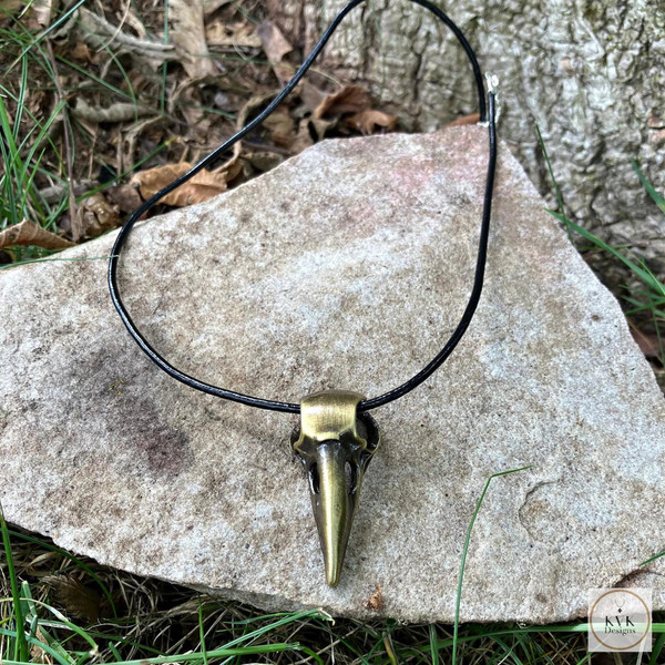 Brass Crow Skull Necklace Pendant sitting on a gray rock