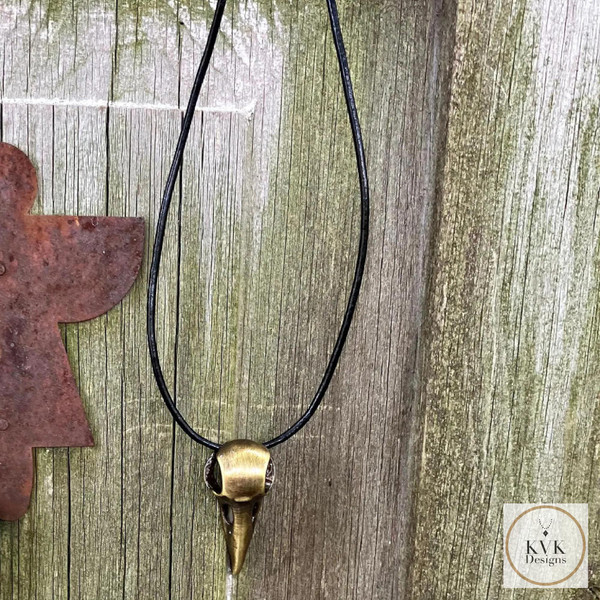 Brass Crow Skull Necklace Pendant hanging from an antique door
