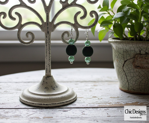 Green Textured Pearl Dangle Earrings shown on an antique earring stand on distressed white table