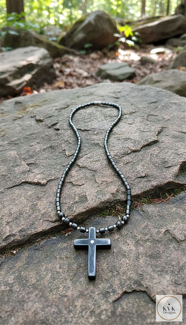 Hematite Believer Cross Necklace laying on rocks outside