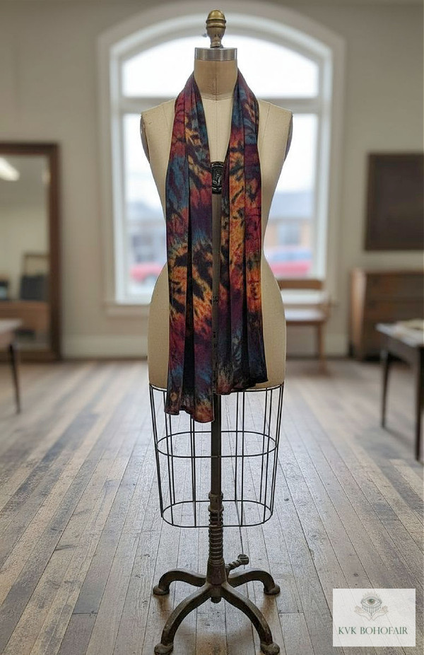 A dress form mannequin displays a colorful, tie-dye scarf in a bright room with wooden floors, large windows, and some furniture in the background.