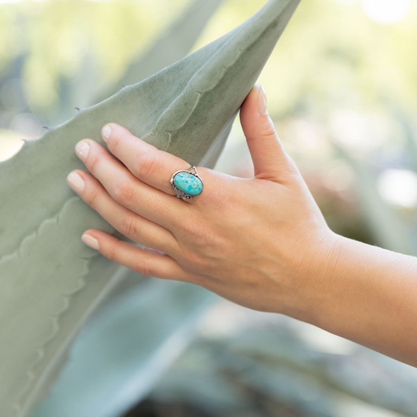 Oval Reconstituted Turquoise Floral Design Ring worn by model holding onto a cactus leaf