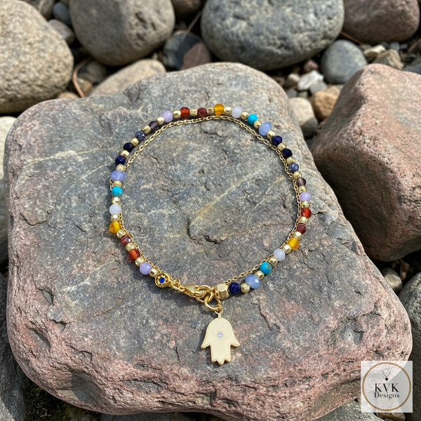 Double Strand Gemstone Hamsa Hand Charm Bracelet laying on a rock outside