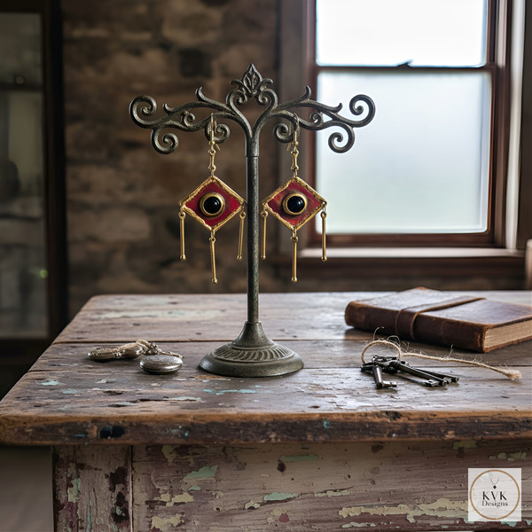 A pair of ornate, red and gold earrings hang on a decorative metal stand atop a rustic wooden table, surrounded by vintage items, including keys, a pocket watch, and a closed book near a window. A pair of ornate, red and gold earrings hang on a decorative metal stand atop a rustic wooden table, surrounded by vintage items, including keys, a pocket watch, and a closed book near a window.