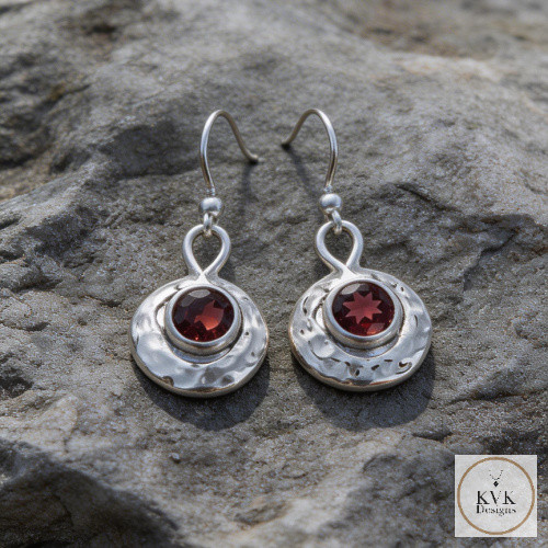 Oxidized Round Hammered Earrings With Garnet laying on rocks outside