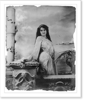 Historic Framed Print, [Young woman modeling: 3/4 lgth., standing by wall, in front of body of water],  17-7/8" x 21-7/8"
