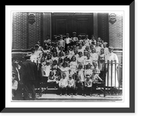 7 rows of children on church steps, Agnes Meyer, when a young woman, standing to right. Sign on church gives Dr. G.G. Maas as pastor, No. 64 7th Street. Another sign refers to undertaker Heritage