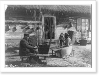 Man and woman making baskets outdoors as small child and others in doorway watch, Poland, Vintage Print