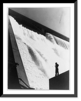 Historic Framed Print, Col[umbia] Basin Proj., Grand Coulee Dam. A workman inspecting the Grand Coulee Dam from the partially-complete training wall near the east powerhouse,  17-7/8" x 21-7/8"