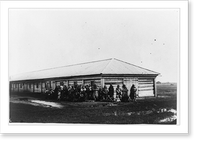 Group of female exiles and their children standing in front of log barracks, Historic Reproduction