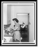 Woman beating eggs in kitchen, and man seated at desk in background, Greenbelt, Maryland, Historic Print