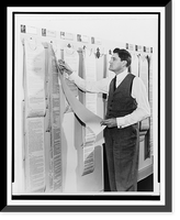 Historic Framed Print, [Eric Sevareid, three-quarter length portrait, standing, facing left, looking at news wire printouts hanging on wall],  17-7/8" x 21-7/8"
