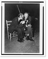 Fiddling Bill Hensley and his rival for Old Time Fiddlers' Championship, Asa Helton, both seated and talking, holding their fiddles, at the Mountain Music Festival, Asheville, North Carolina Time
