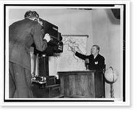 Frazier Hunt, seated at desk, pointing to a wall map of Africa, cameraman filming him in left foreground, Antique Poster
