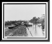 Workers unloading sandbags from flatbed railroad car, while others are building a levee, partially submerged electric power line poles on right.Ewing, Inc., Baton Rouge. Classic, Historic Print