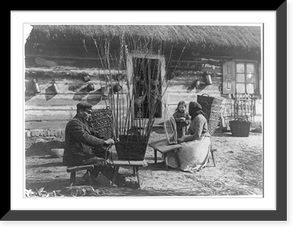 Man and woman making baskets outdoors as small child and others in doorway watch, Poland, Vintage Print