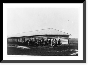 Group of female exiles and their children standing in front of log barracks, Historic Reproduction