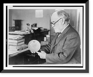 Dr. J. Walter Fewkes, seated at desk, facing left, examining disk showing figure entering maze, Vintage Poster