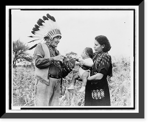 Mrs. Marion John Miles holding baby, while Oneida Chief William H. Rockwell demonstrates how stripes on squash determine the celebration of the gathering of the harvest, Oneida Lake, New York Cla