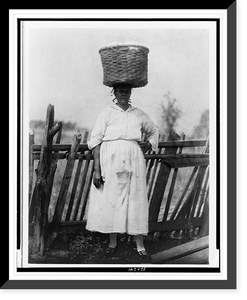 African American woman standing by wooden fence, with basket on her head, Vintage Print