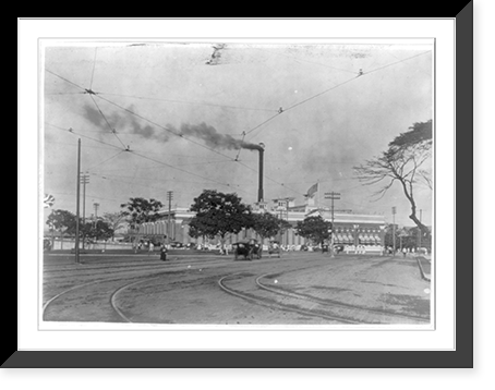 American military installations and activities in the Philippine Islands, ca. 1885 to 1925: Street scene, showing people, carriages and a rather large building, with a smoke stack smoking Timeles
