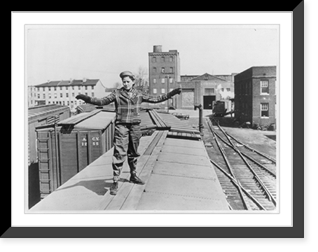 Mrs. Elizabeth McDevitt, a brakeman on a U.S. railroad at an Atlantic Coast embarkation port, standing on top of a freight car, signals the locomotive driver and other train crew members Classic