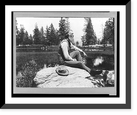 John Muir, full-length portrait, facing right, seated on rock with lake and trees in background, Historic Reproduction