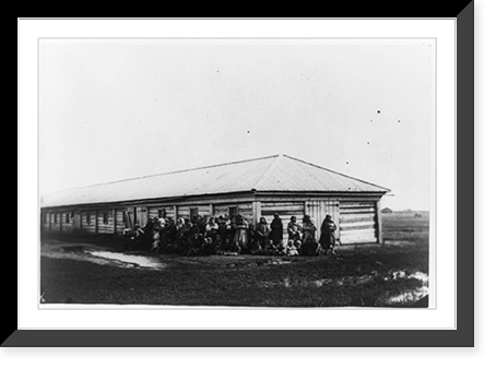 Group of female exiles and their children standing in front of log barracks, Historic Reproduction